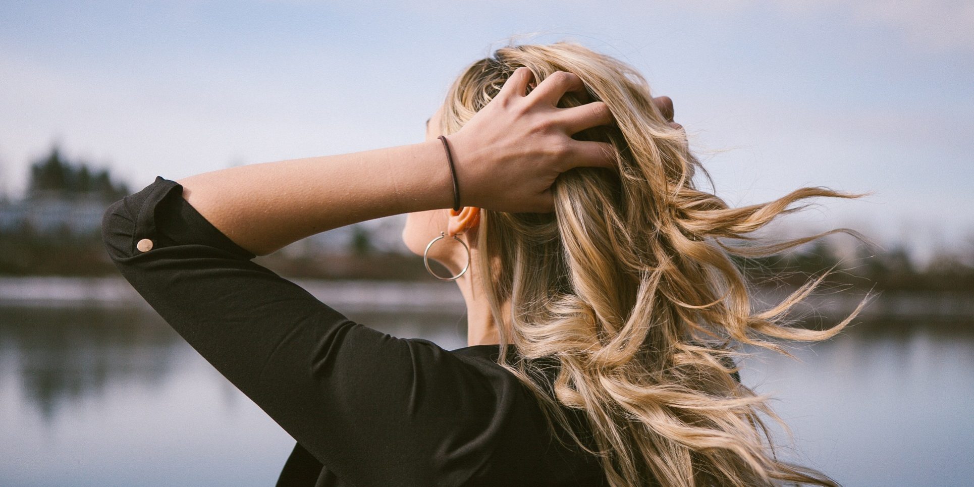 femei, par, inamici O femeie isi trece mainile prin par cu fata spre lac