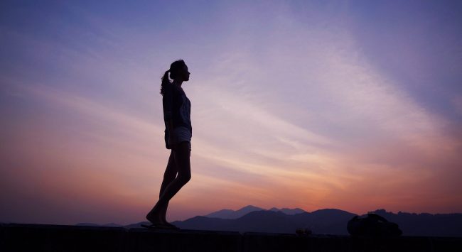 Femeie sta in picioare sub cer in apus