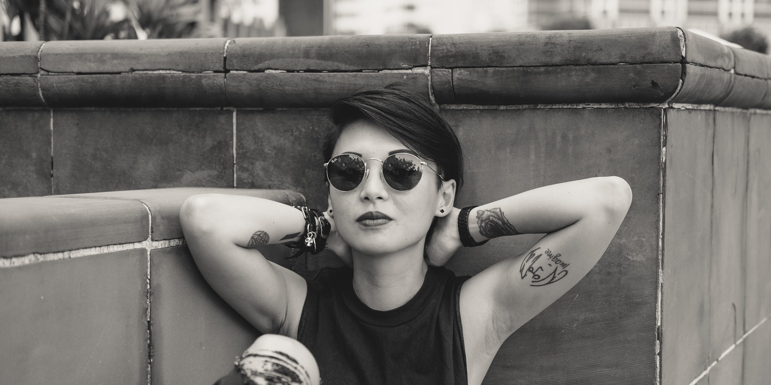 O fata cu ochelari de soare sta rezemata de un perete.