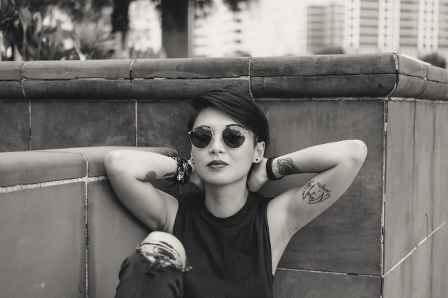 O fata cu ochelari de soare sta rezemata de un perete.