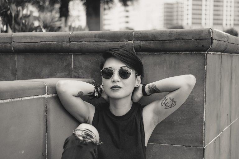 O fata cu ochelari de soare sta rezemata de un perete.